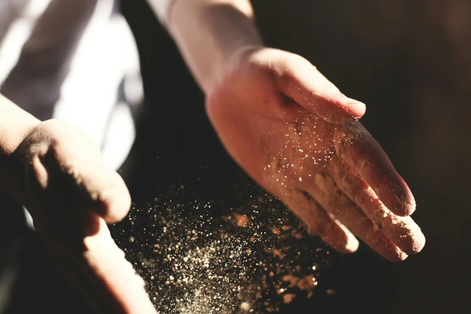 A person’s hands create a cloud of dust as they rub together, with sunlight illuminating the particles floating in the air A person’s hands create a cloud of dust as they rub together, with sunlight illuminating the particles floating in the air