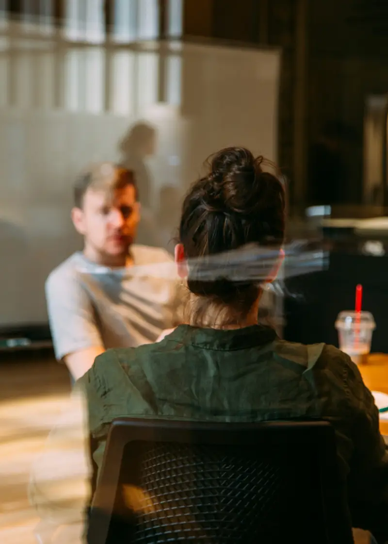 A woman with a bun hairstyle sits at a table in a meeting room, engaged in conversation, with a beverage beside her A woman with a bun hairstyle sits at a table in a meeting room, engaged in conversation, with a beverage beside her